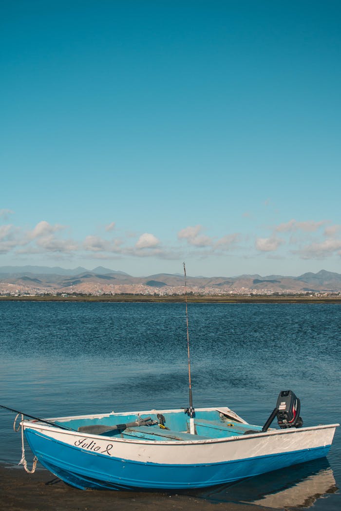 about-01 A small motorboat rests peacefully on calm bay waters with scenic hills in the background.