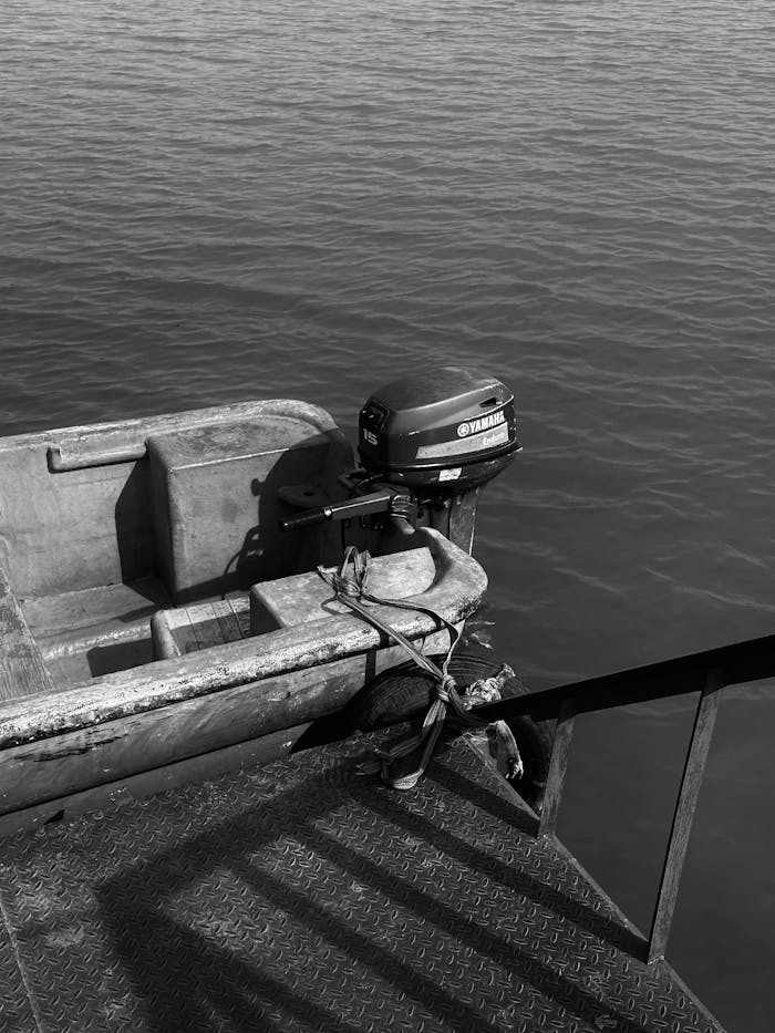 Black and white photo of an empty vintage boat tied to a dock on calm waters.