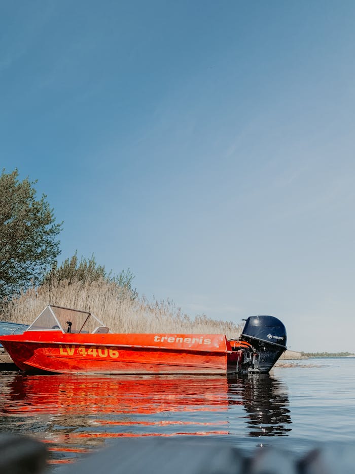 gallery-1 A vivid red motorboat reflecting in a serene lake, surrounded by nature under a clear sky.